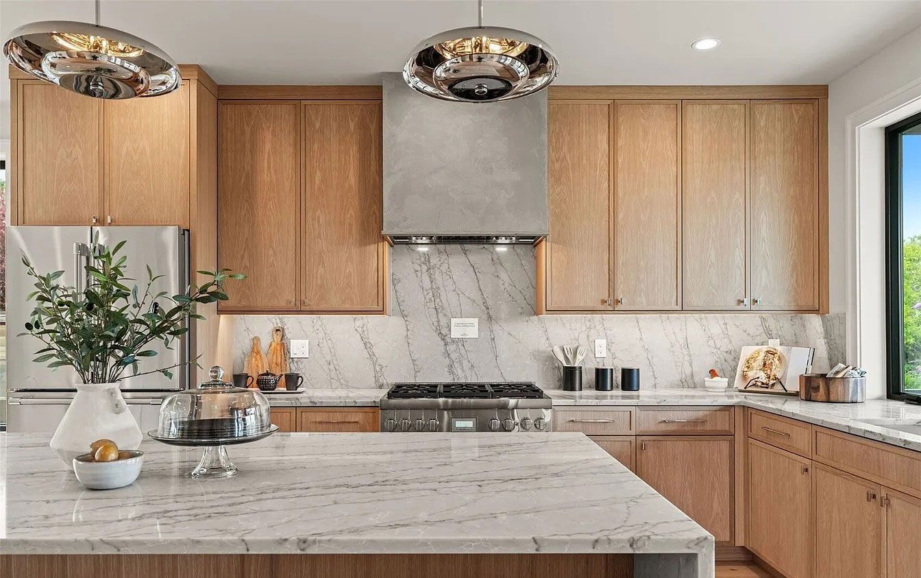 Modern kitchen with wood cabinets, gray marble island, stainless range hood, and pendant lights