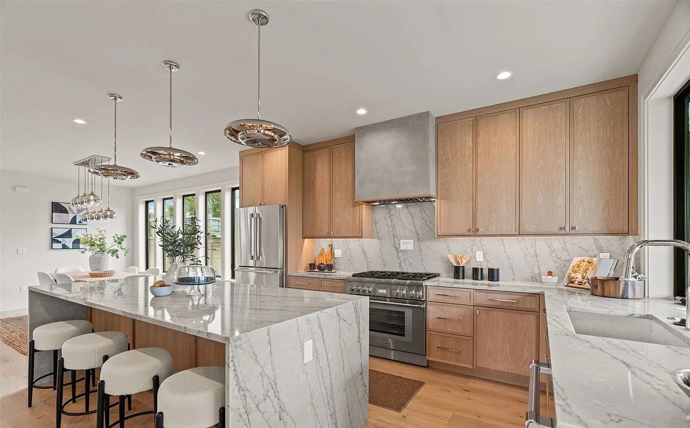 Modern kitchen with white marble island, wood cabinets, pendant lights, and bar stools.
