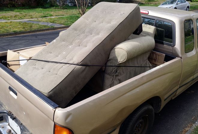 Tan pickup truck loaded with a couch, mattress, and a large foam block in the bed