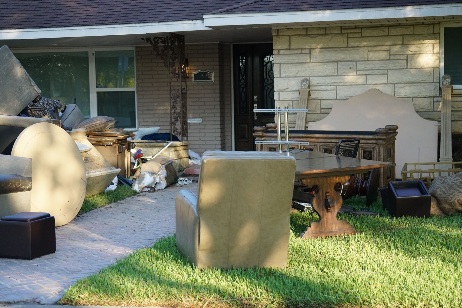 Cluttered front porch with furniture, boxes, and household items outside a brick house