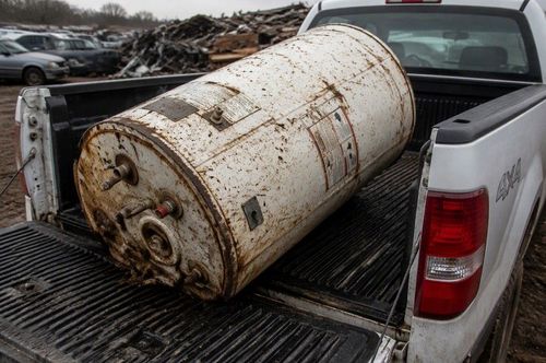 Rusty white metal tank in the bed of a pickup truck in a junkyard