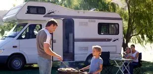 Happy father and son grilling their food in front of a motor home