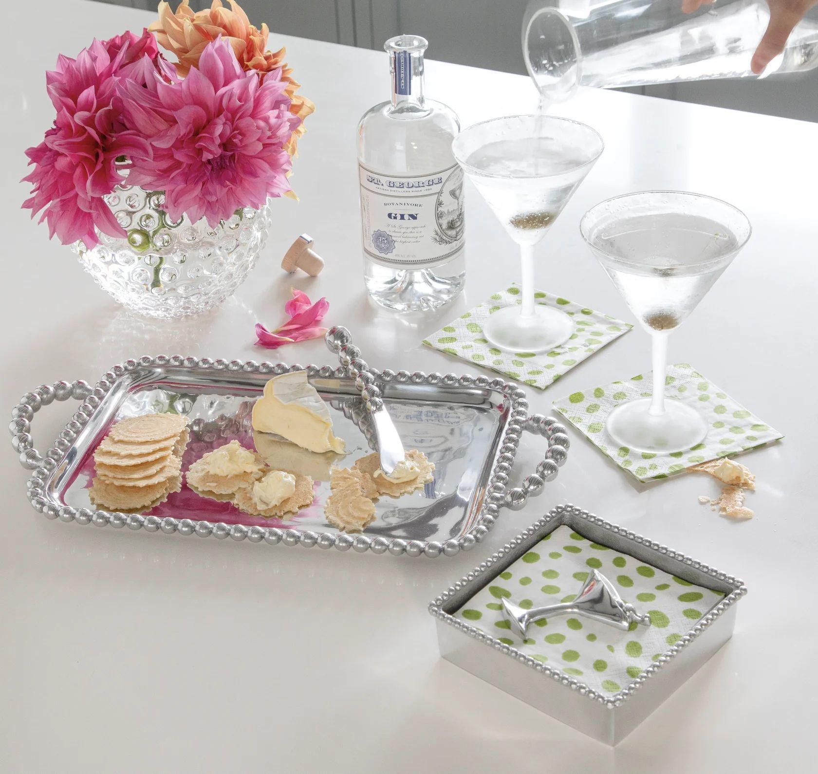 A table with a tray of crackers , a bottle of vodka , and two martini glasses.
