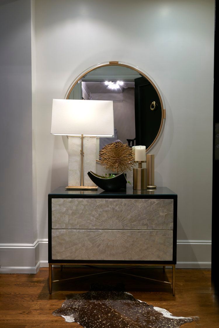 A dresser with a lamp and a mirror in a hallway.