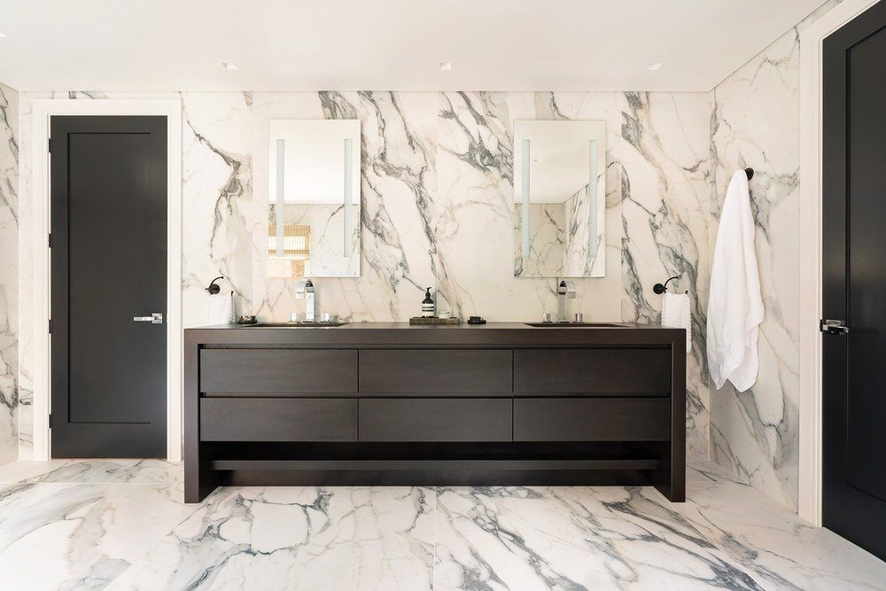 A bathroom with two sinks , two mirrors and marble walls.