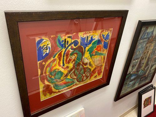 A painting is hanging on a wall next to other paintings.