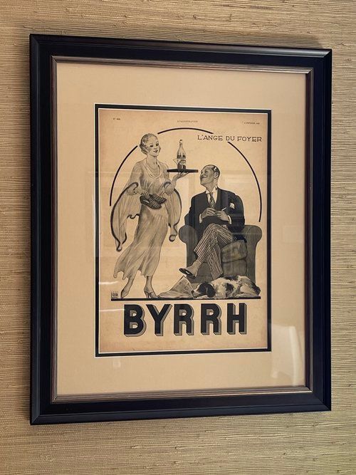 A framed picture of a man sitting in a chair and a woman holding a tray with the word byrrh on it