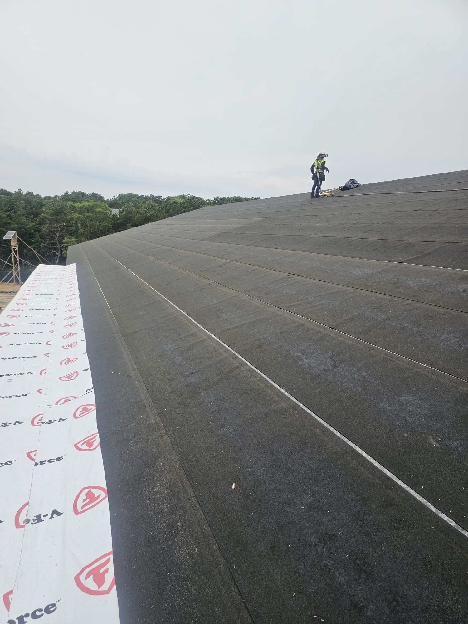 A man is standing on top of a large black roof.