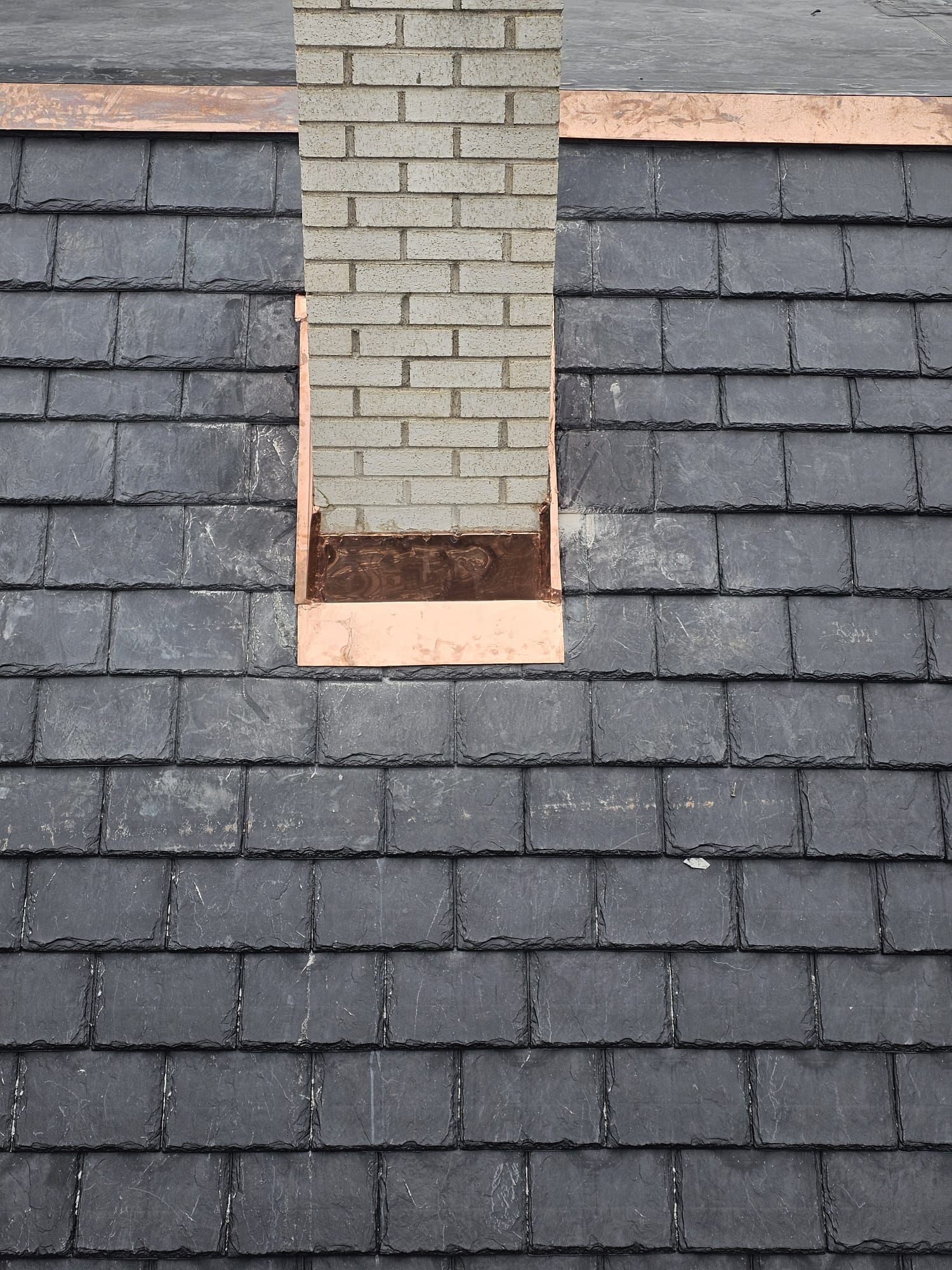 A brick chimney on top of a slate roof