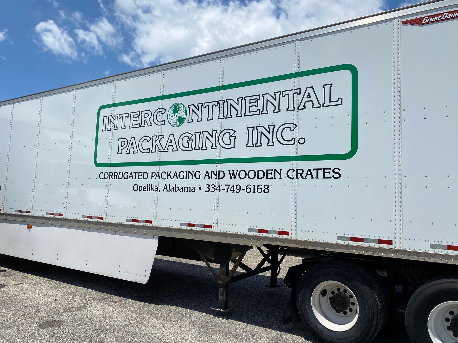 A white semi truck with a green sign that says Interc International Packaging Inc.