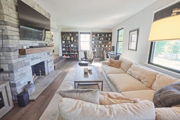 Bright living room with a stone fireplace, beige sectional sofa, coffee table, and large windows.