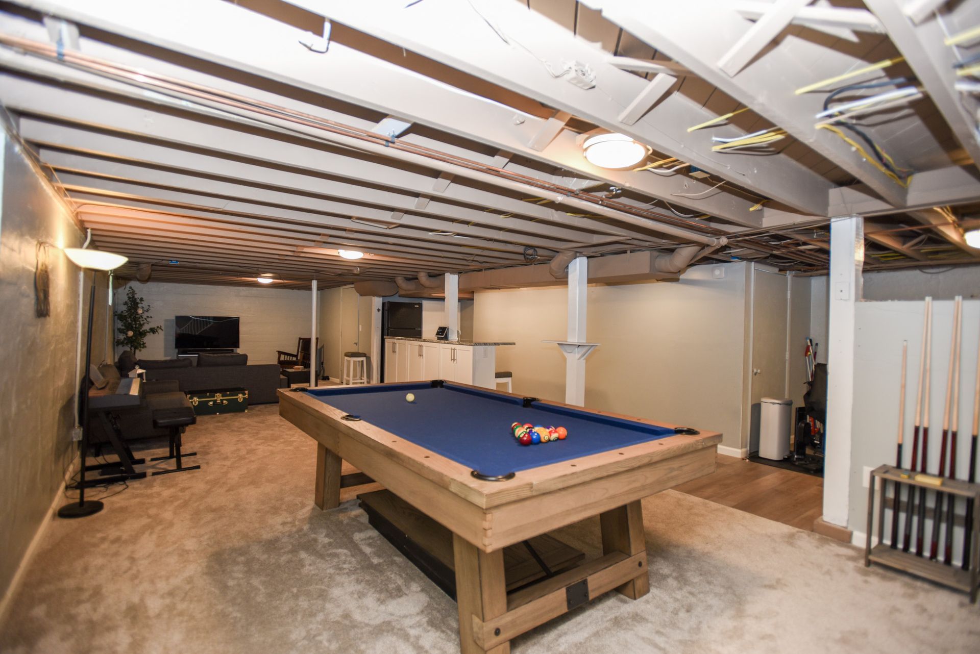 Basement game room with pool table, concrete floor, exposed ceiling, and bar stools along the wall.