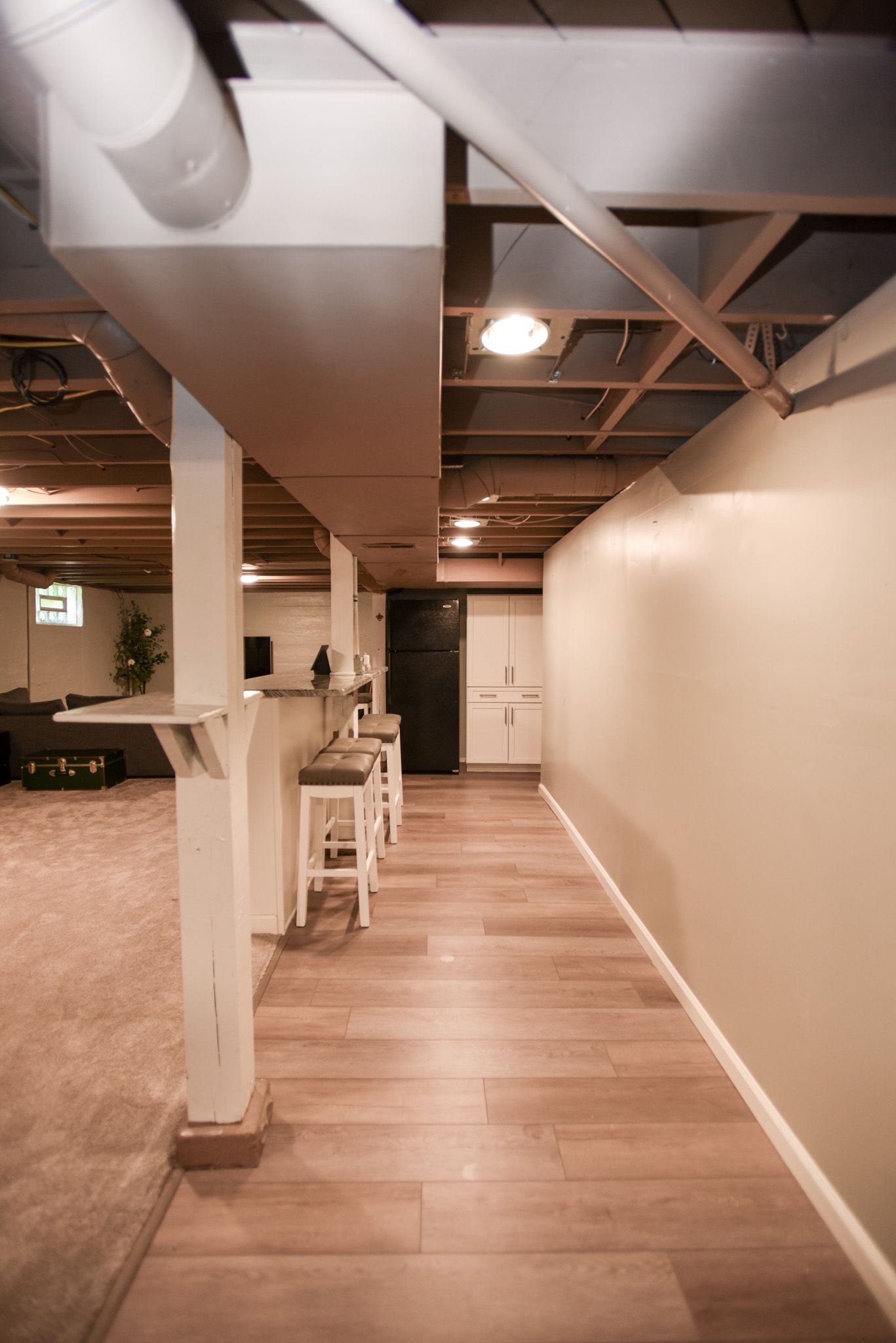 Long hallway with wood flooring, white walls, exposed ceiling beams, and bar stools along the left side.