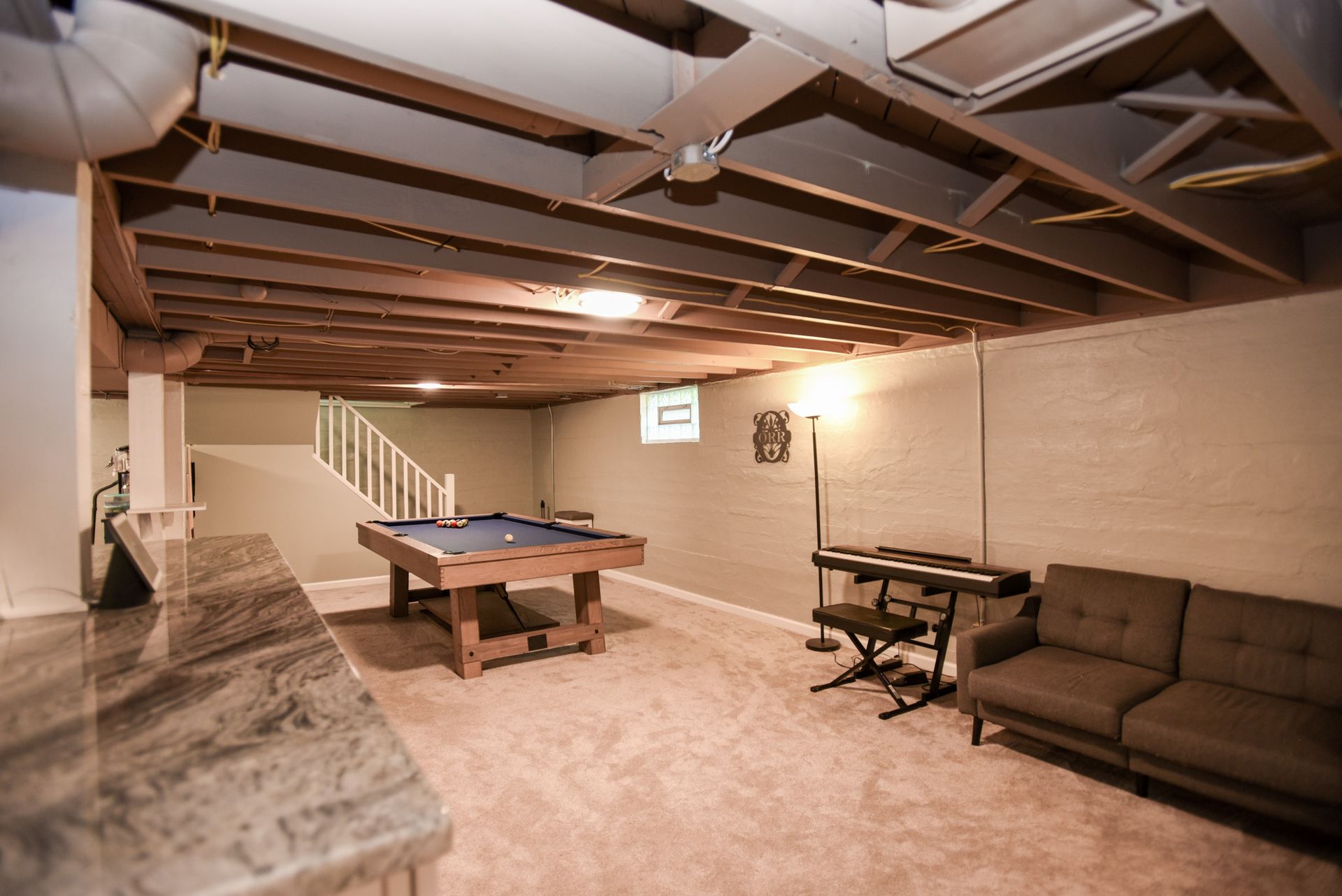 Basement rec room with pool table, sofa, keyboard, and exposed ceiling beams.