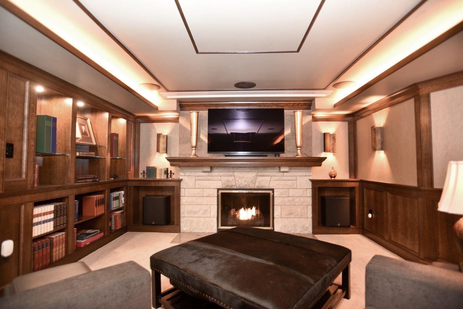 Modern living room with built-in wood shelves, fireplace, TV, and a large ottoman.