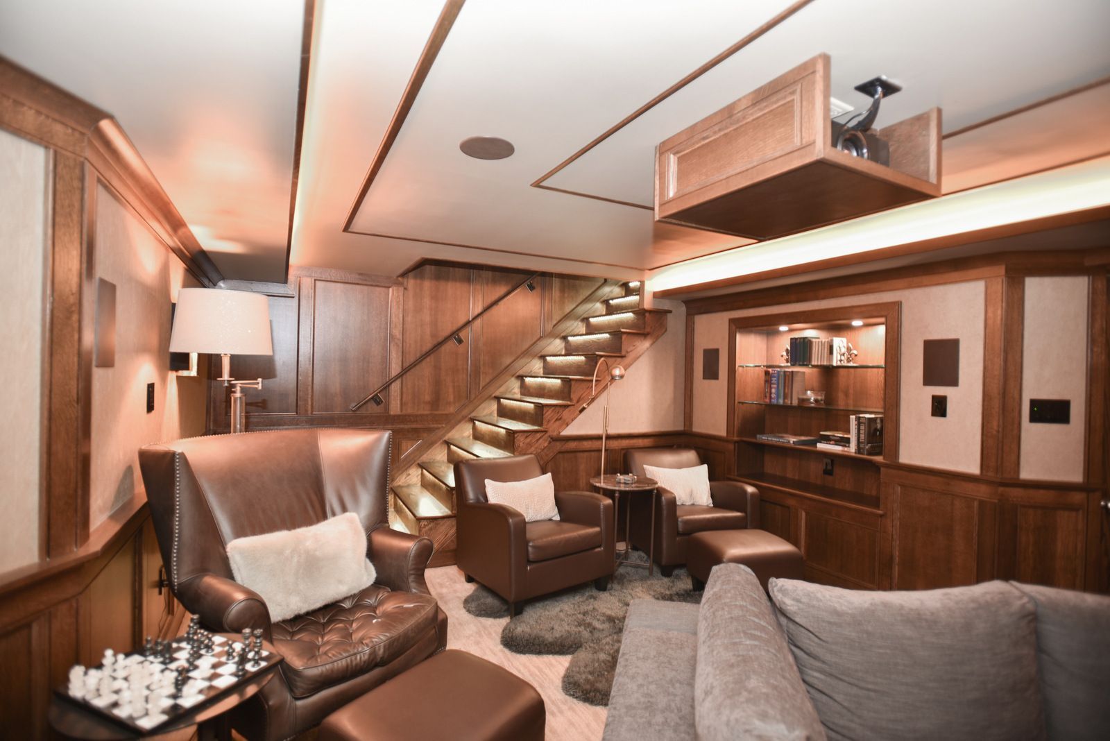 Wood-paneled cabin lounge with sofas, armchair, staircase, and loft seating area.