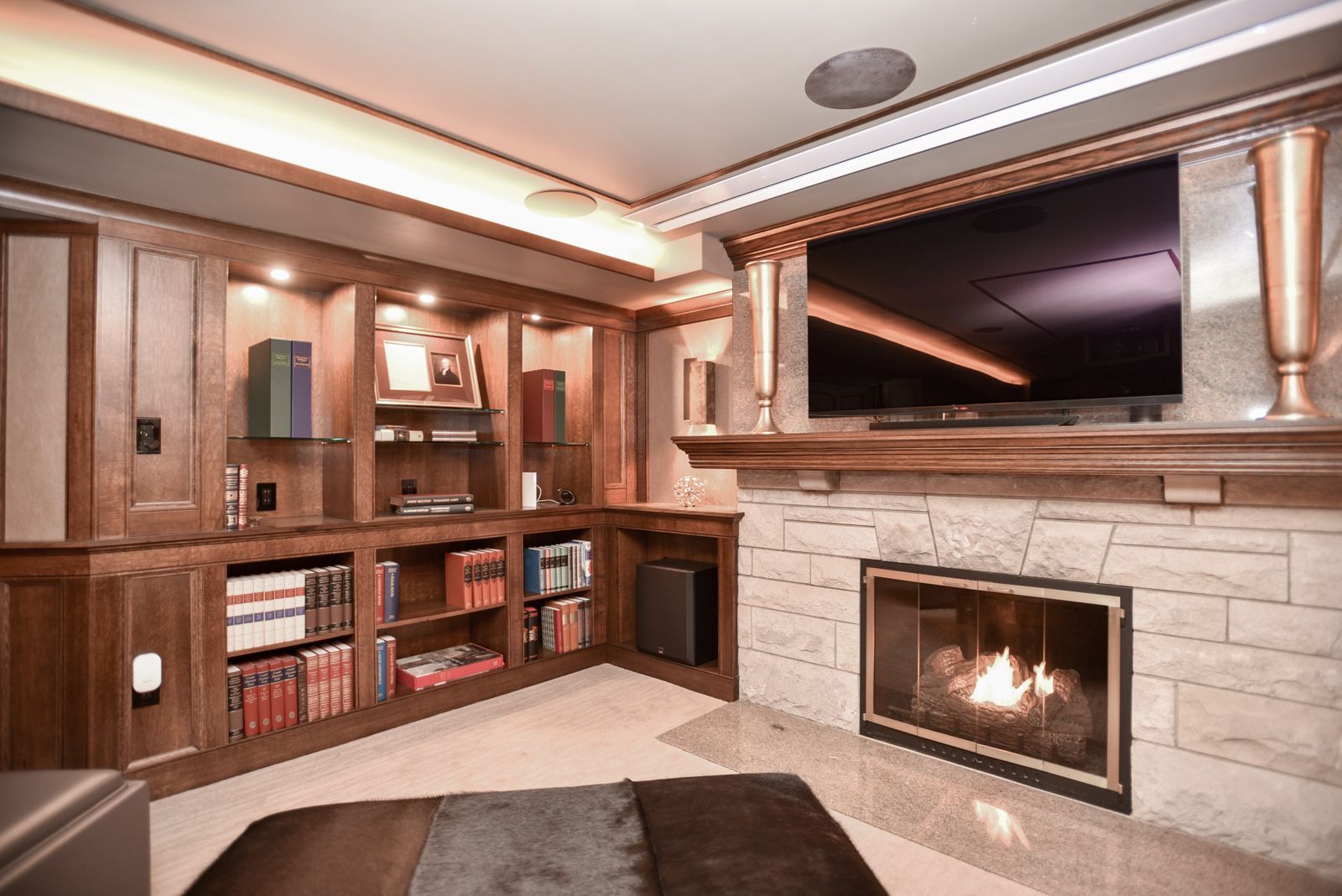 Modern living room with built-in wood shelving, stone fireplace, and a large wall-mounted TV.