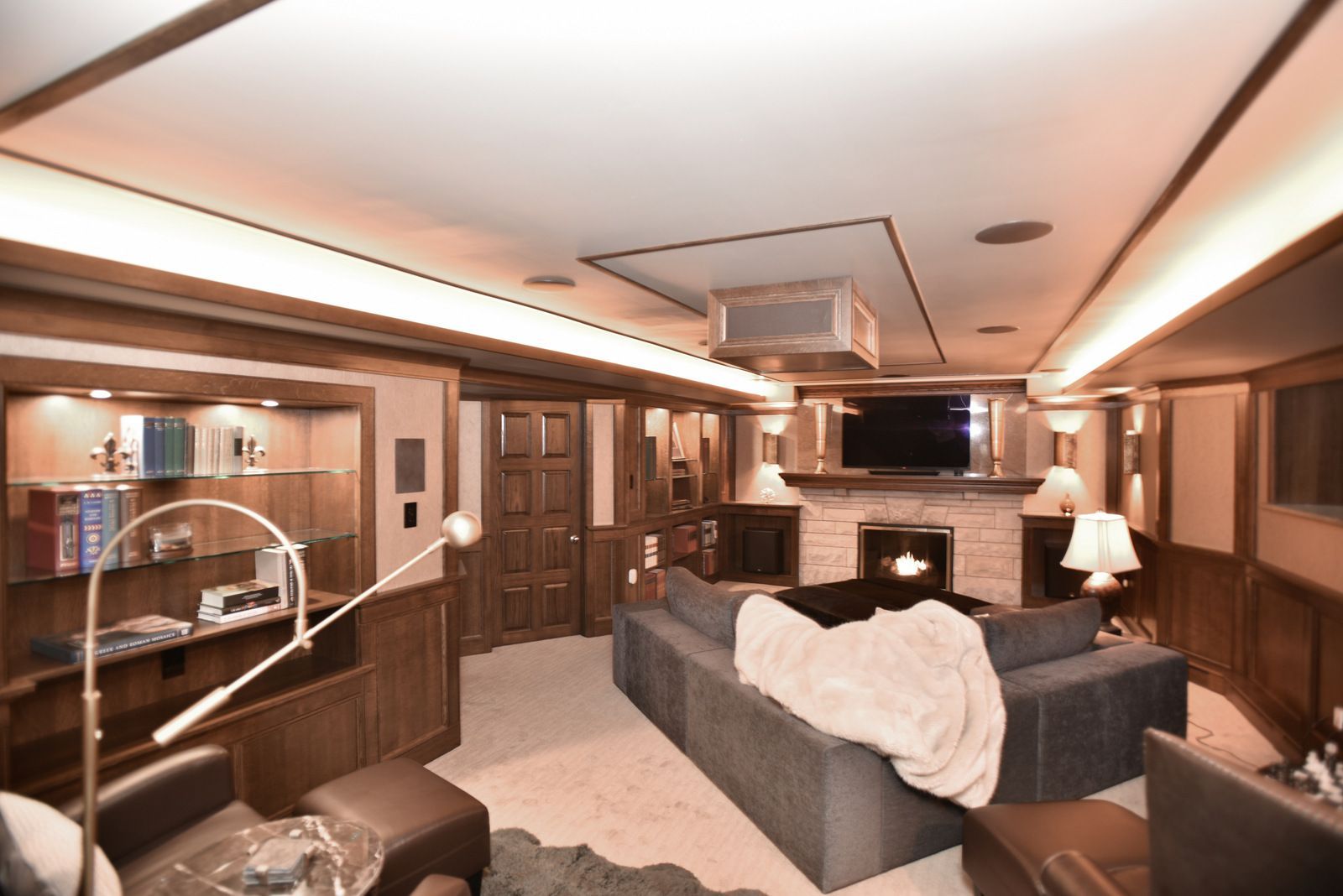 Cozy wood-paneled living room with a gray sectional, fireplace, lamp, and large wall mirror.