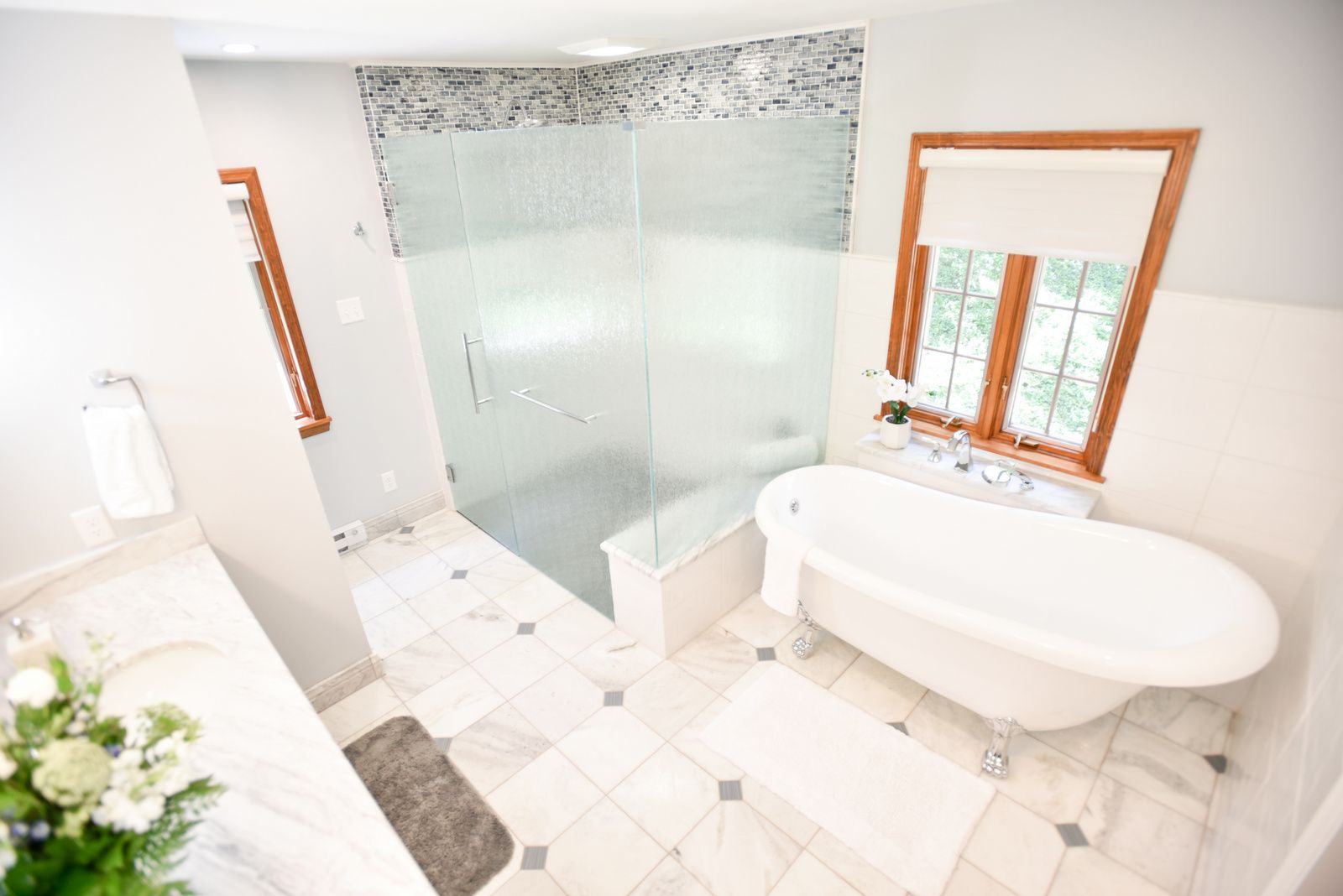 Bright modern bathroom with glass shower, freestanding white tub, and mosaic tile floor.