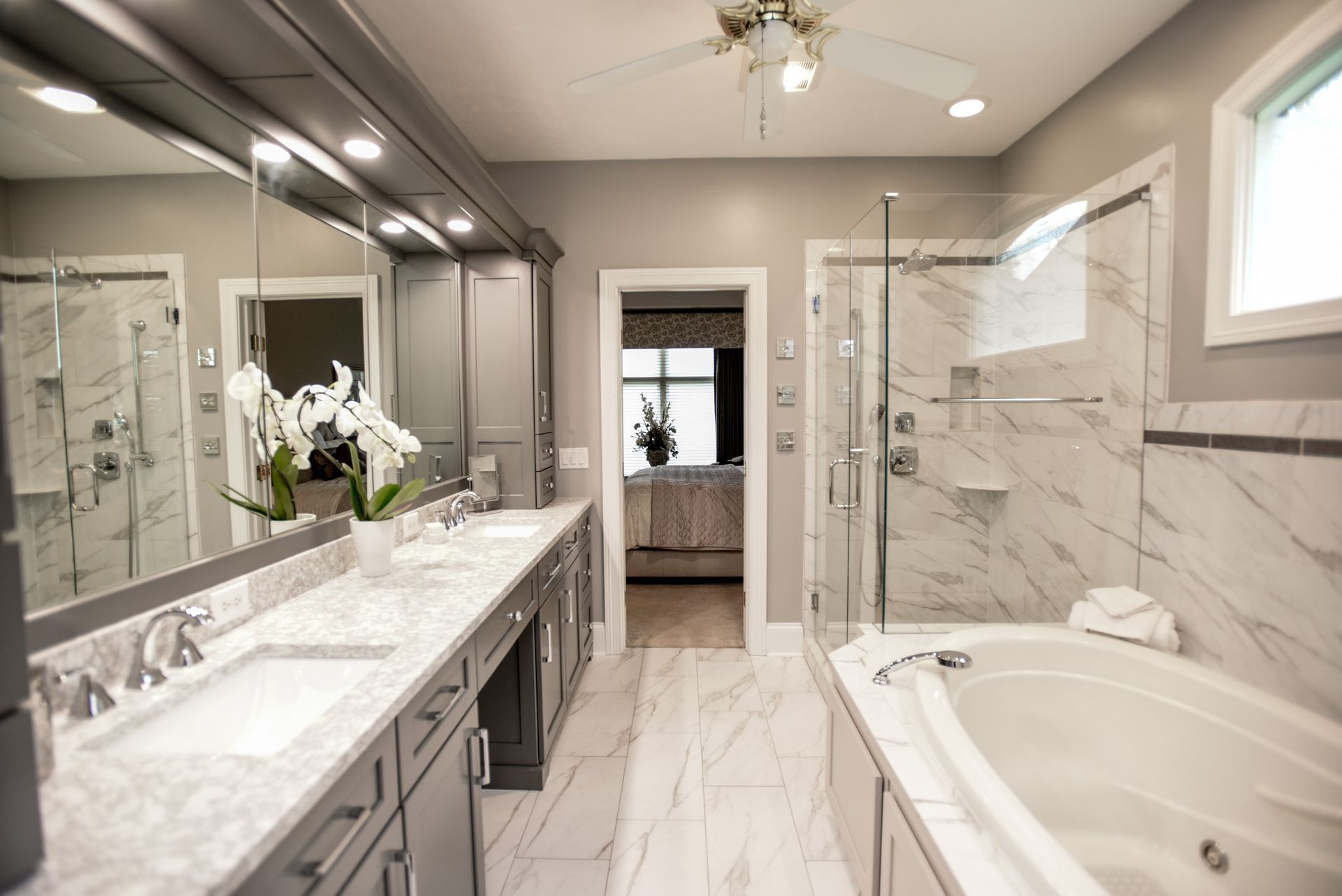 Bright modern bathroom with marble vanity, large mirror, glass shower, and soaking tub.