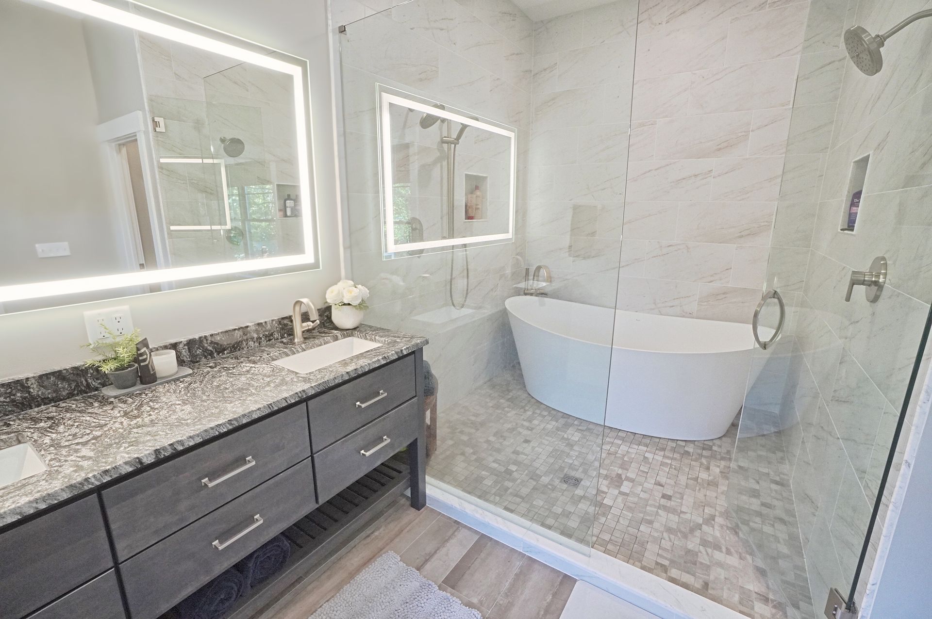 Modern bathroom with double vanity, backlit mirrors, soaking tub, and glass shower.