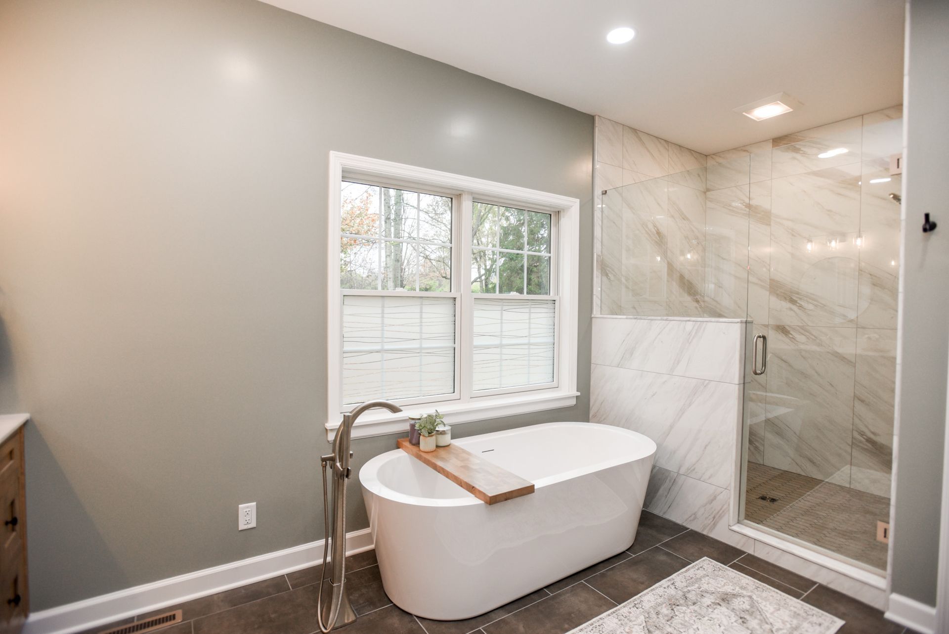Modern bathroom with freestanding tub, walk-in shower, and window with white shutters.