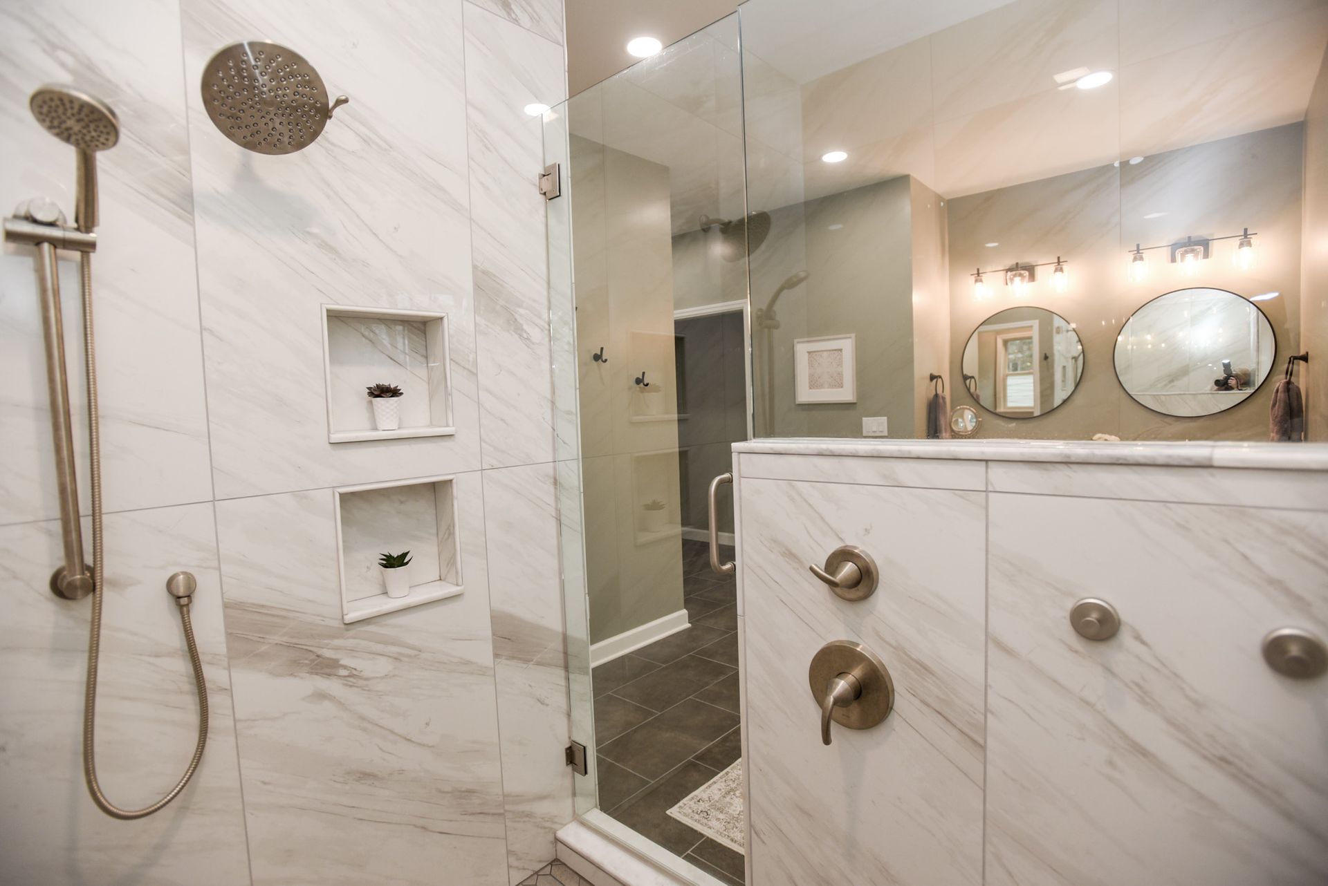 Modern marble bathroom with walk-in shower, handheld showerhead, glass partition, and vanity with double mirrors.