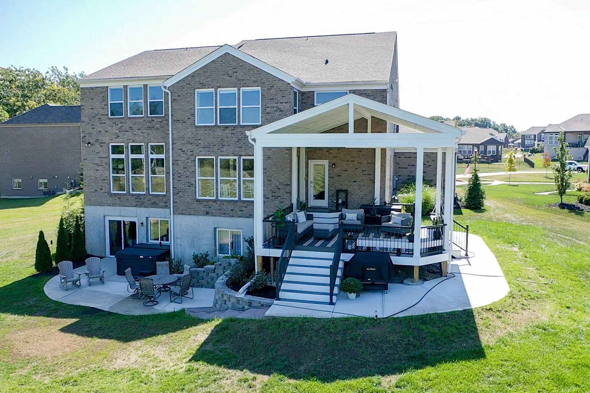 Backyard view of a two-story brick house with a covered patio and lawn beyond.