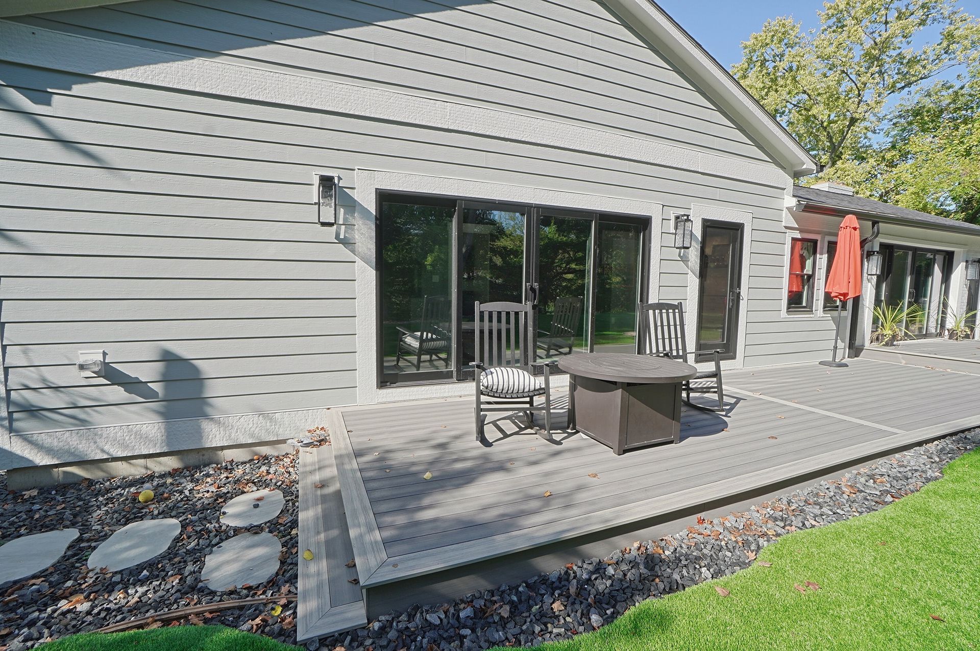 Back patio with gray siding, sliding glass doors, outdoor chairs, and a fire pit on a wooden deck.