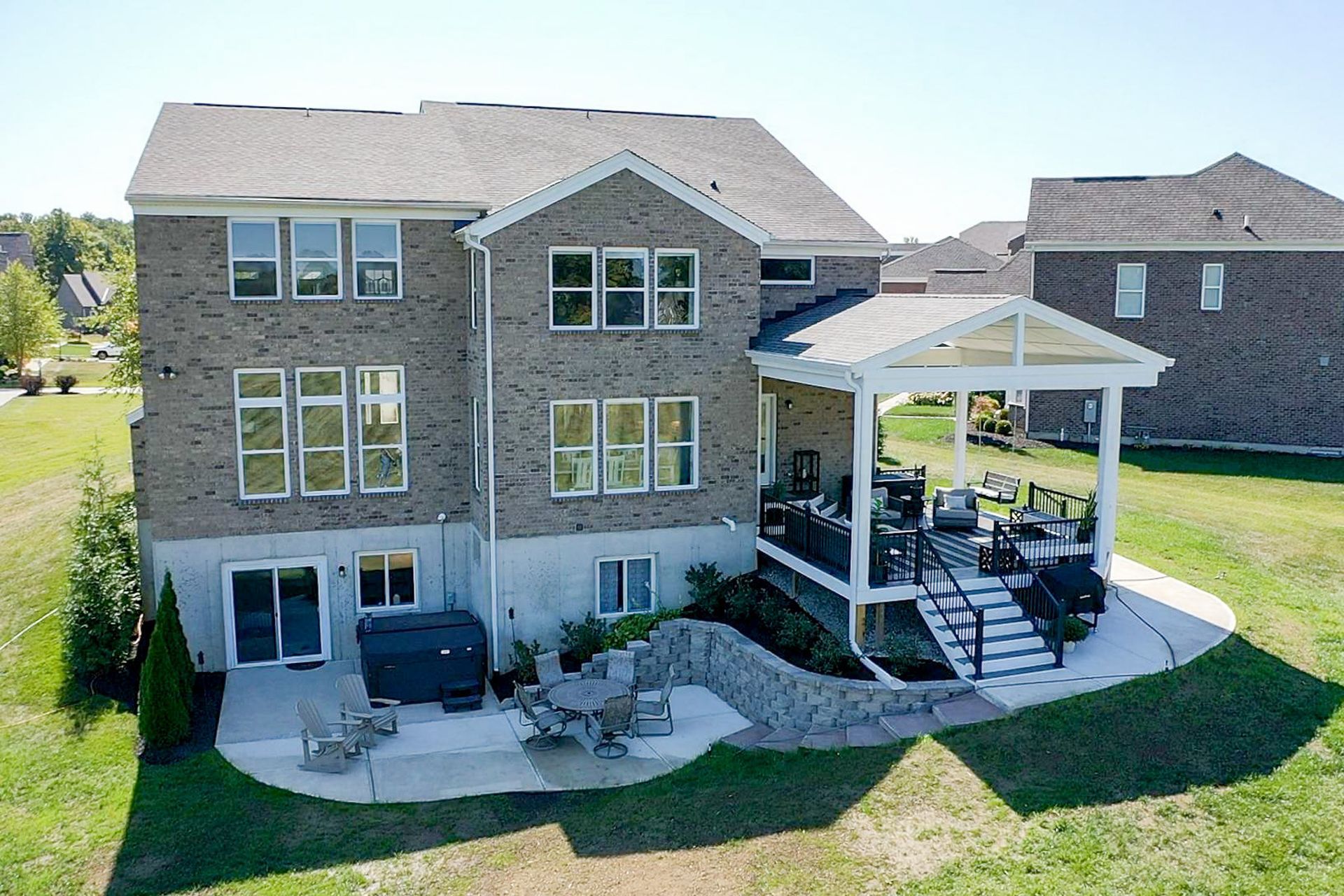 Backyard view of a gray brick house with a screened porch, patio furniture, and a manicured lawn.