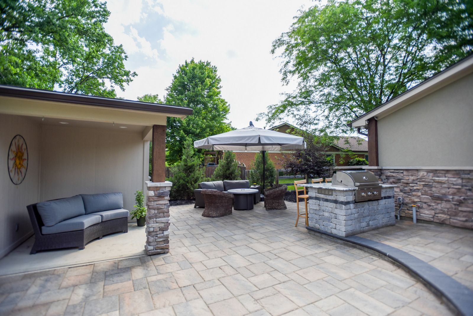 Covered patio with gray seating, fire pit table, and stone outdoor kitchen under umbrellas.