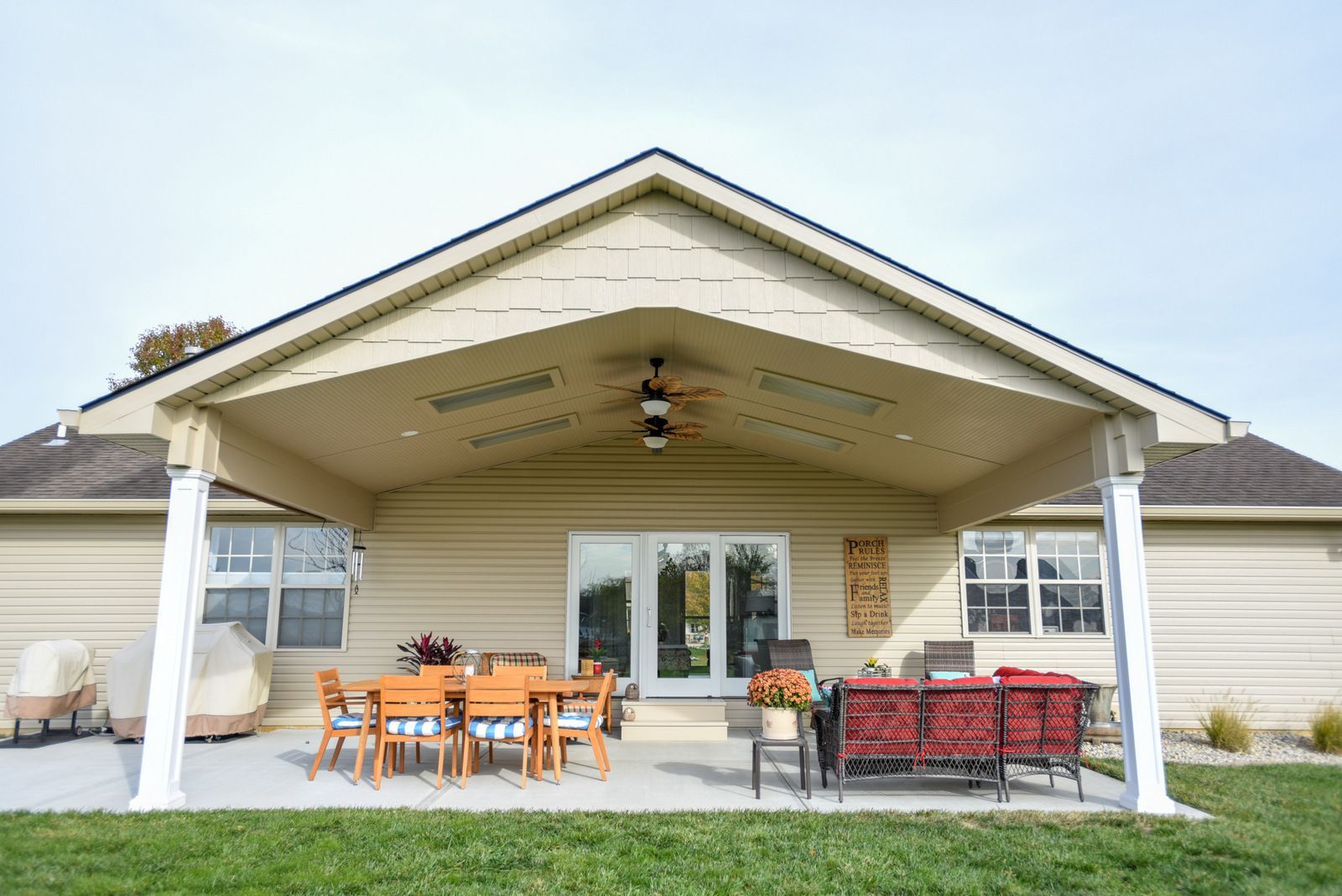 Covered patio with outdoor dining table, red seating, and ceiling fans on a beige house.