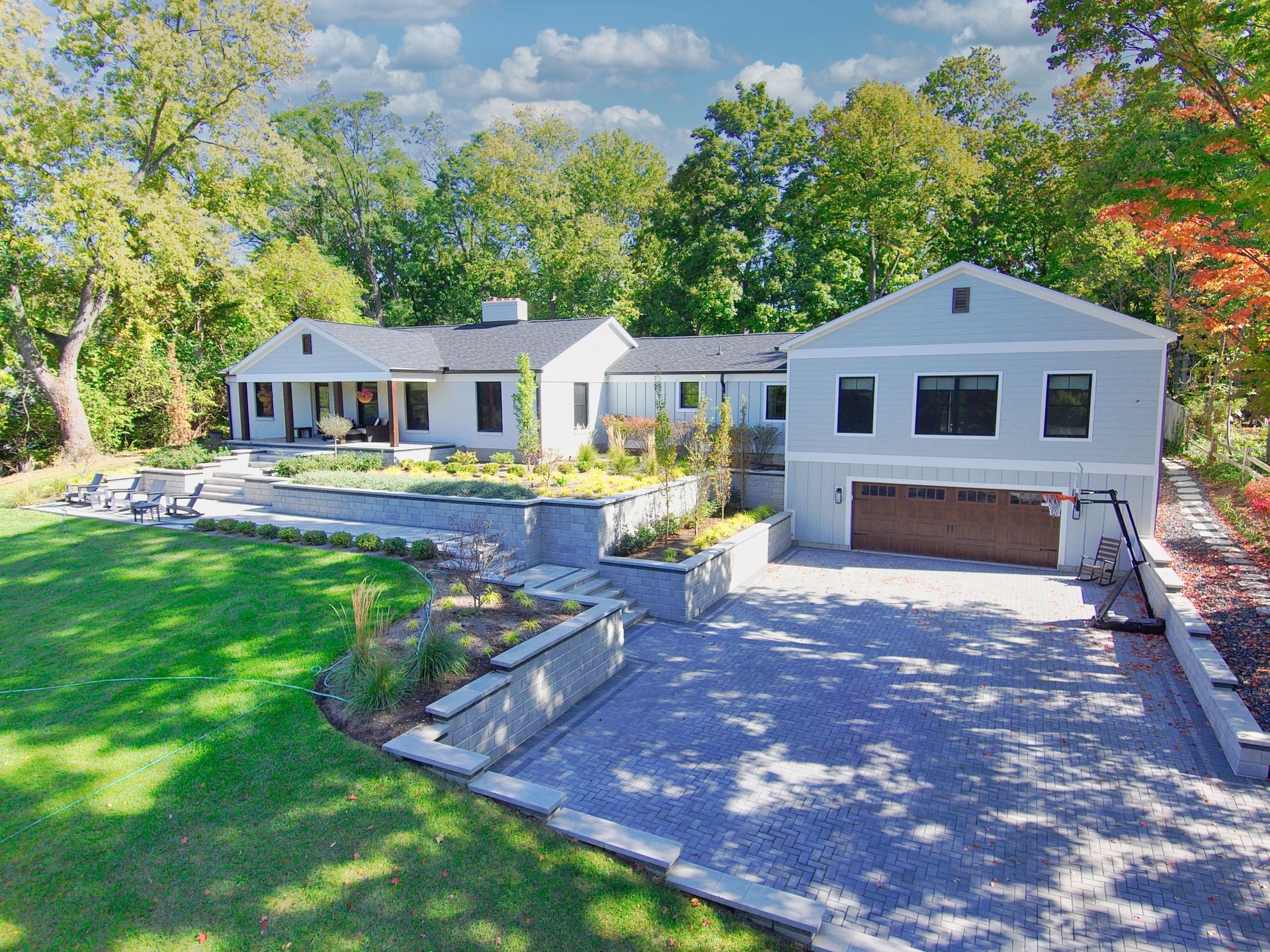 Modern white house with a garage, stone driveway, and lush green lawn surrounded by trees.