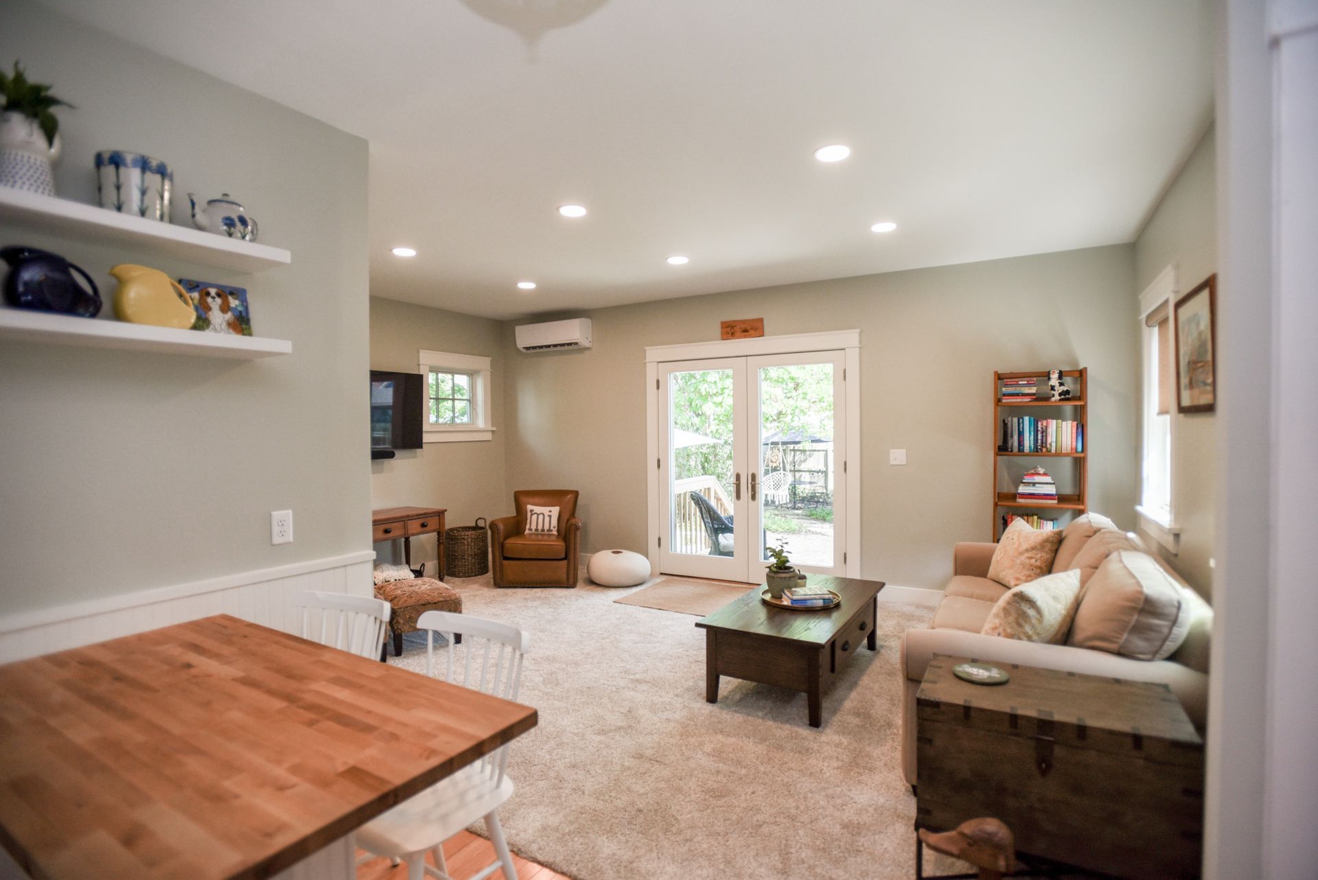 Bright living room with beige sofas, coffee table, built-in shelves, and glass doors to a patio.