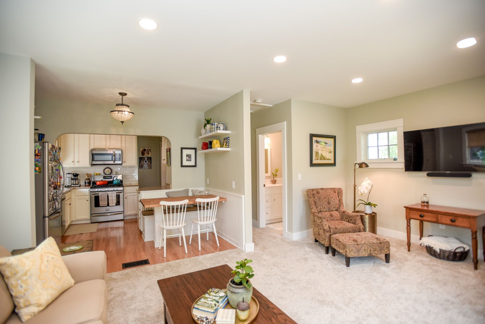 Bright living room and kitchen with beige walls, white dining table, armchair, and wood accents.