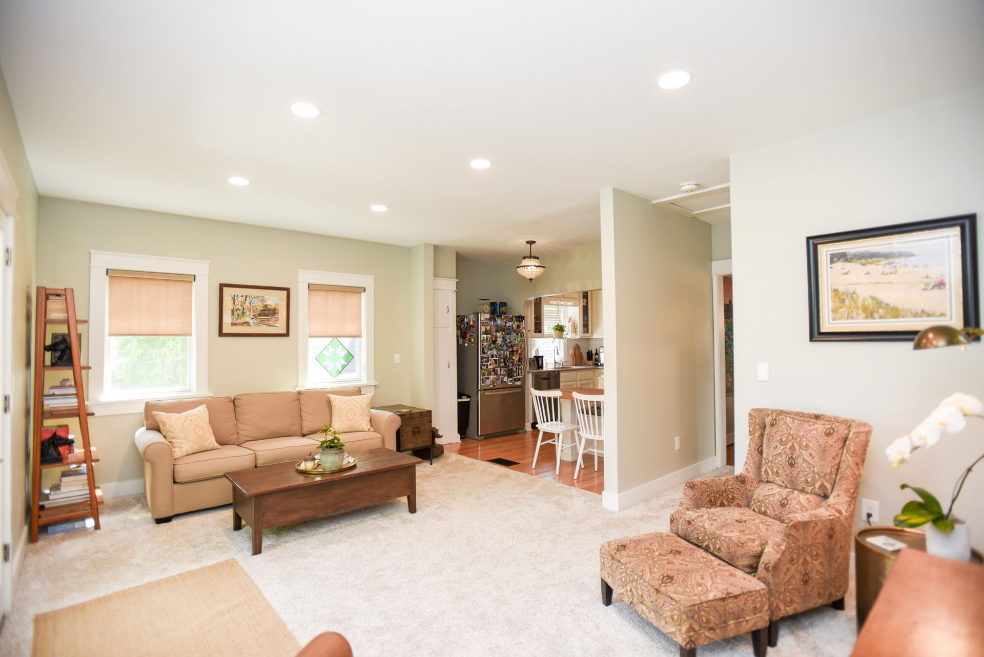 Bright living room with beige sofa, patterned chair, coffee table, and recessed ceiling lights.