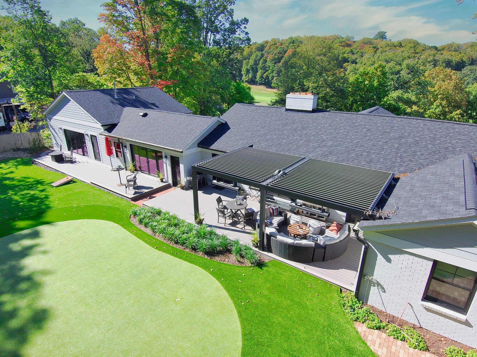 Aerial view of a modern house with gray roof, striped patio awning, and a green backyard patio.