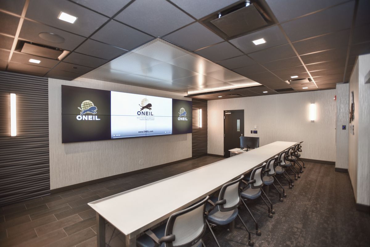 Modern conference room with long white table, chairs, wall screens, and dark ceiling lighting.