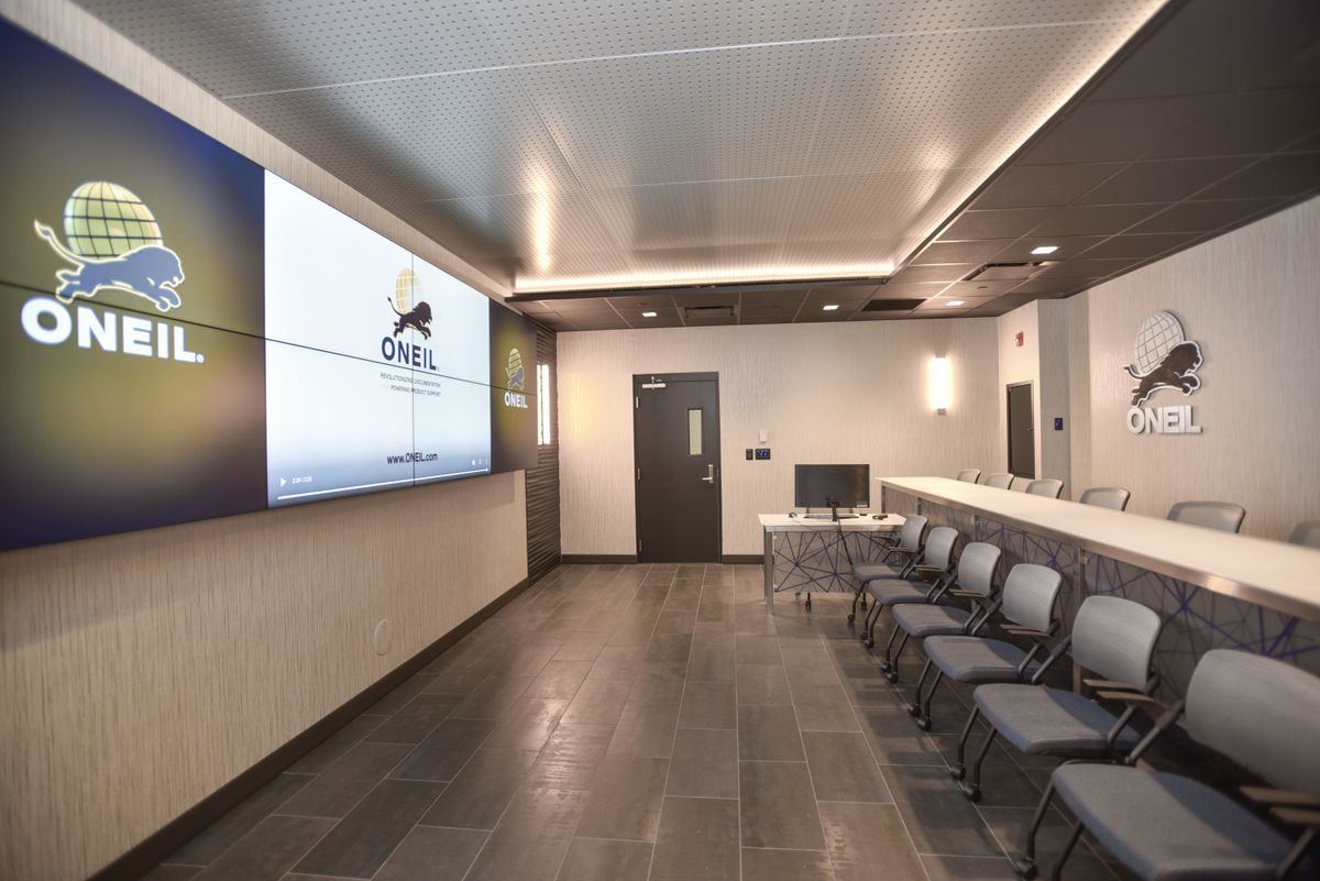 Modern waiting room with rows of gray chairs, wall-mounted screen, and branded “ONEIL” signage.