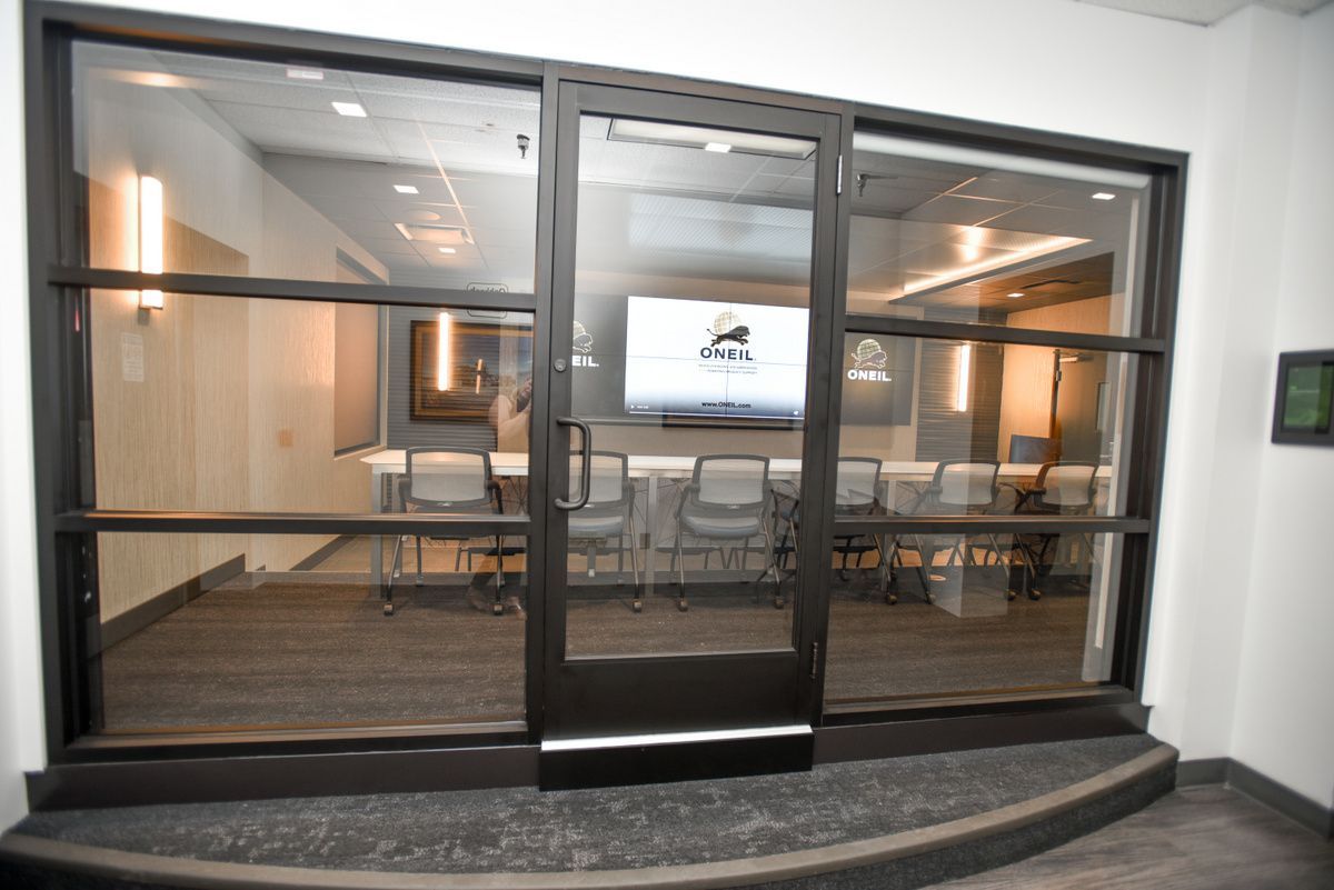 Glass-walled conference room with a long table, chairs, and a wall-mounted screen.
