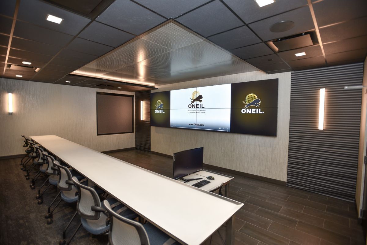Modern conference room with long white table, black chairs, and wall screens displaying O’Neill branding.