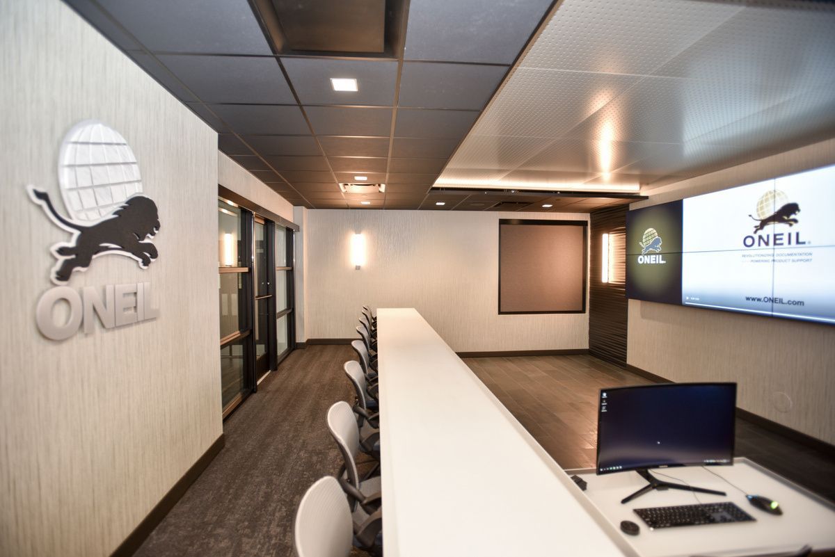 Modern office reception area with white counter, chairs, shelves, and O’NEIL signage on the wall.