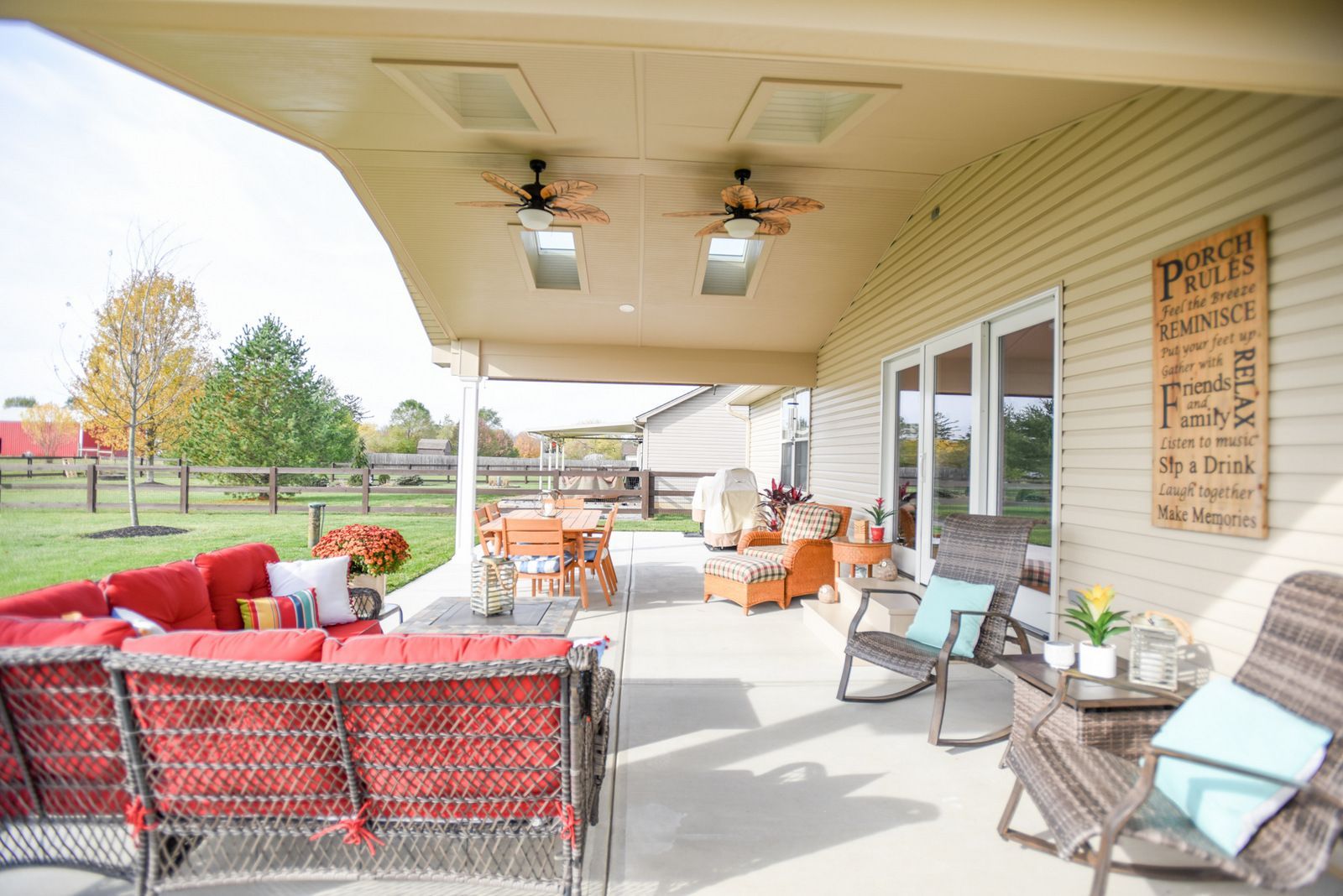 Covered outdoor patio with red and white seating, ceiling fans, and sliding glass doors overlooking a lawn.