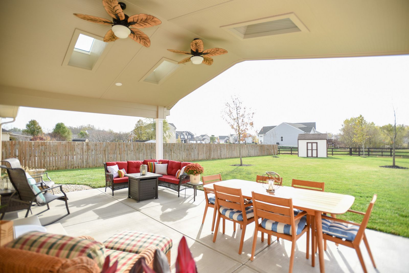 Covered patio with outdoor seating, dining table, and ceiling fans overlooking a grassy backyard.