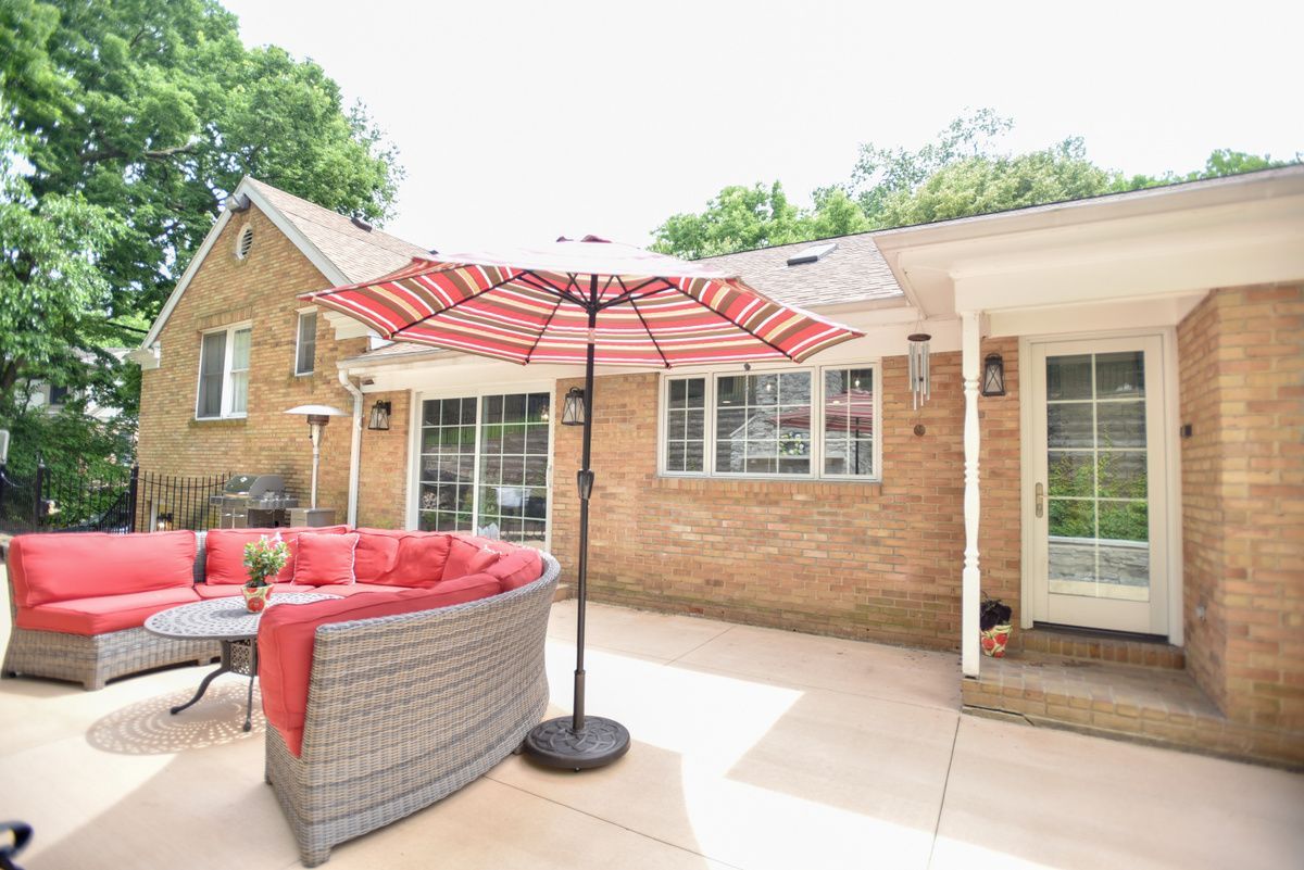 Patio with red-cushioned outdoor seating, striped umbrella, and brick house exterior.