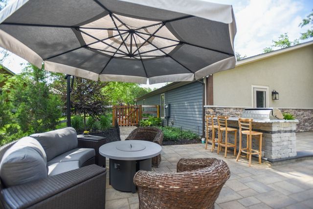 Patio seating area with gray sofa, wicker chairs, large umbrella, and outdoor bar beside a house