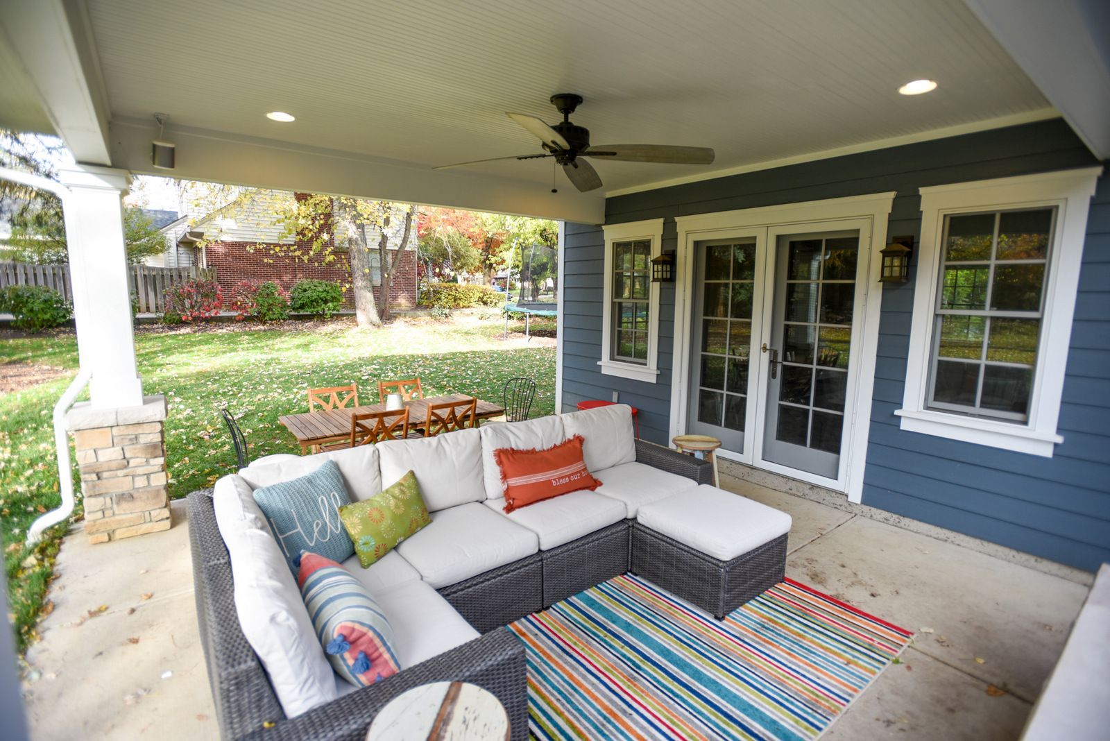Covered patio with sectional sofa, colorful rug, and French doors overlooking a garden.