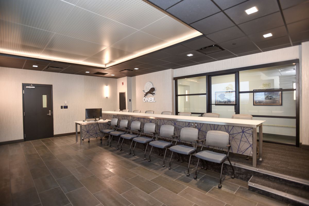 Empty modern waiting area with rows of gray chairs, a counter, and glass office windows.