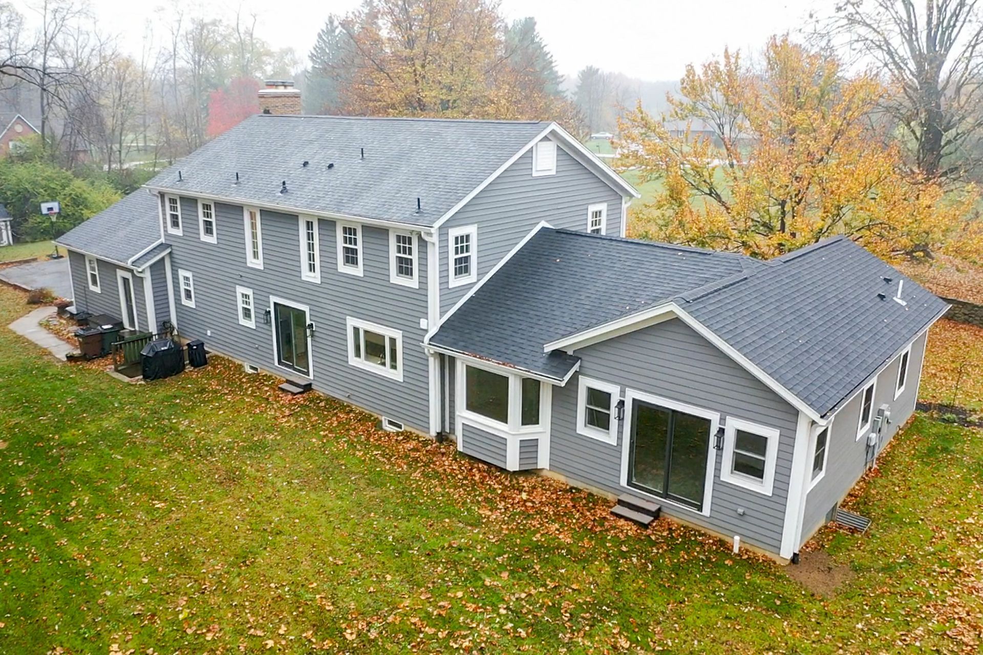 Gray house with white trim and a gabled roof on a leafy lawn in autumn.
