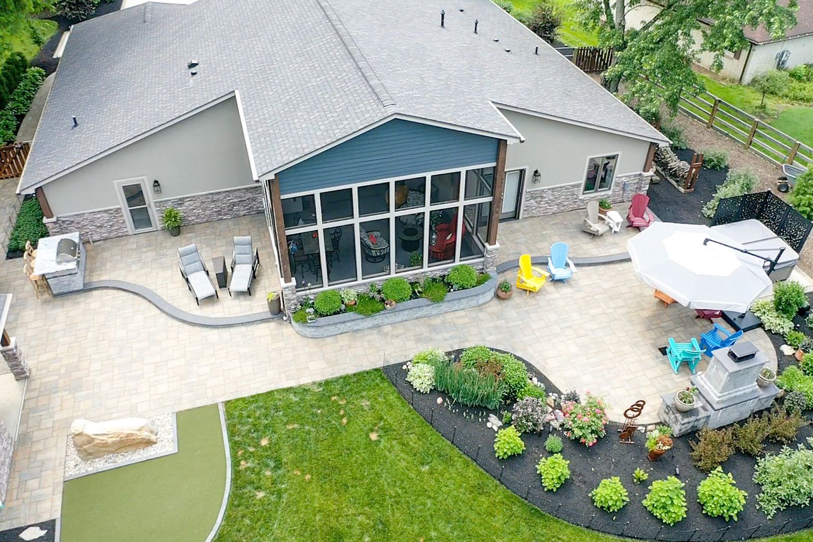 Aerial view of a backyard patio with a house, screened windows, lawn, potted plants, and outdoor seating.